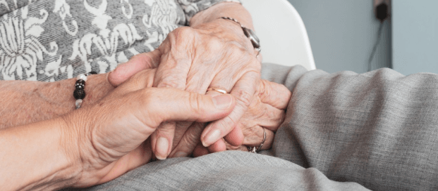 Image of a caregiver holding the hands of an older adult who requires in-home care.