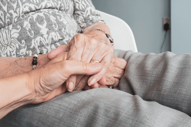 Image of a caregiver holding the hands of an older adult who requires in-home care.