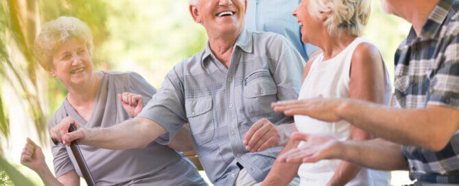 A caregiver in a blue top smiles with a group of seniors enjoying time together outdoors during a respite care stay.